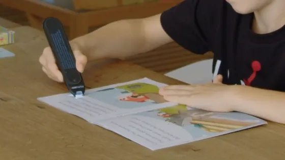 A child with dyslexia using a standalone assistive reading pen independently on a printed storybook
